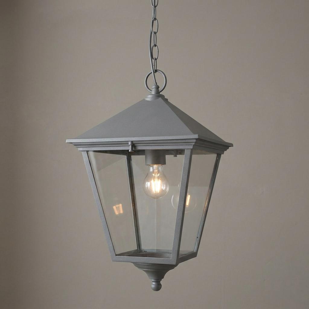 Classic black outdoor lantern pendant light with clear glass panels and a lit bulb hanging against a plain wall.