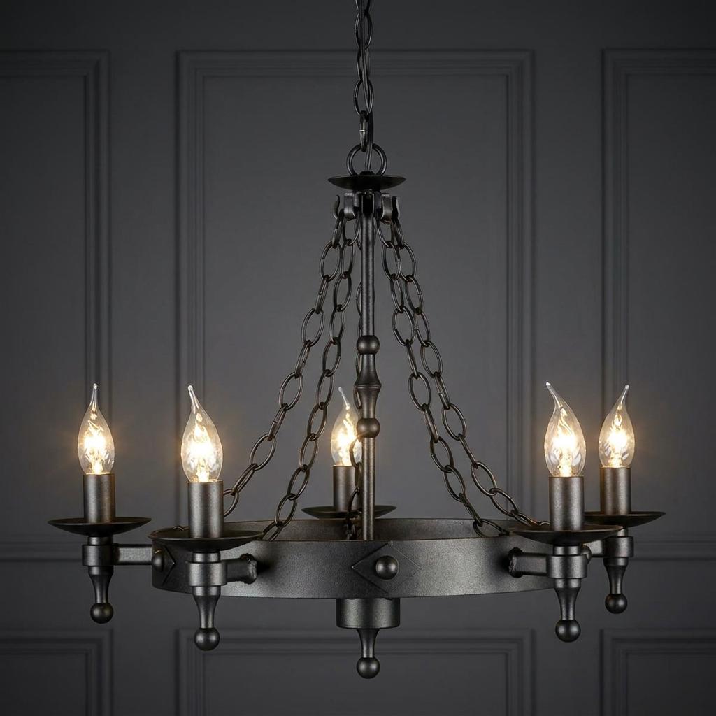 A medieval-style Elstead Warwick Graphite 5 Light Chandelier with candle bulbs against a dark paneled wall.