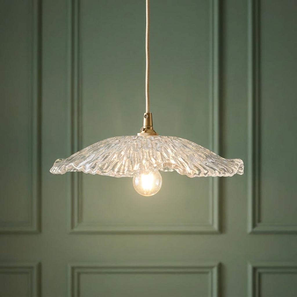 Textured ruffled glass pendant light with brass fixture and braided cable against a green paneled wall.