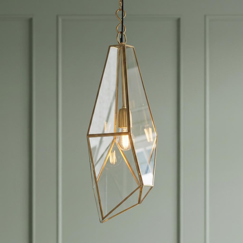 An antique brass geometric glass pendant light illuminated against a green paneled wall.