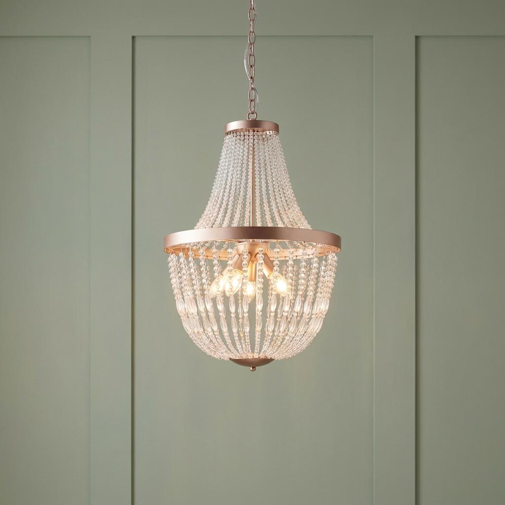 Endon Celine 5 Light rose gold chandelier with glass bead strands hanging against a sage green paneled wall.