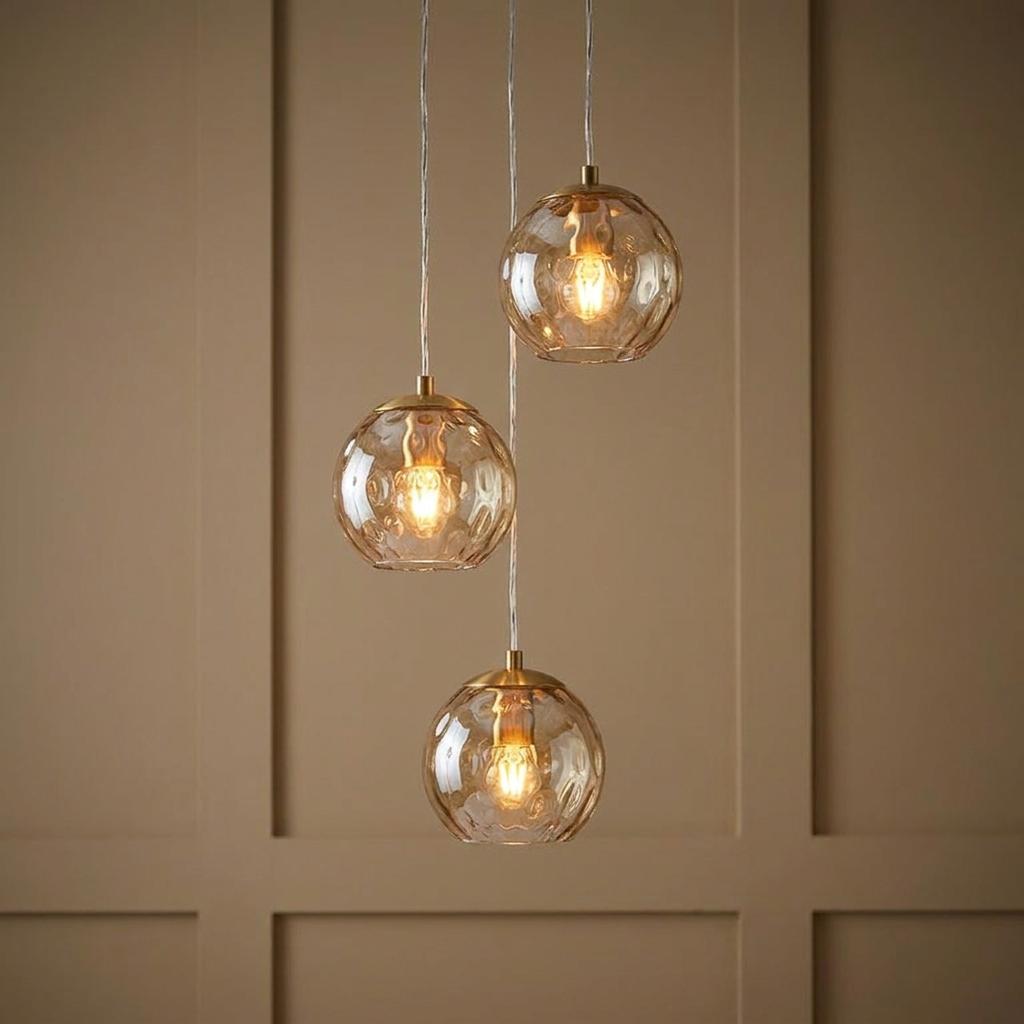 Three brass pendant lights with dimpled champagne glass shades hanging at staggered heights against a paneled wall.
