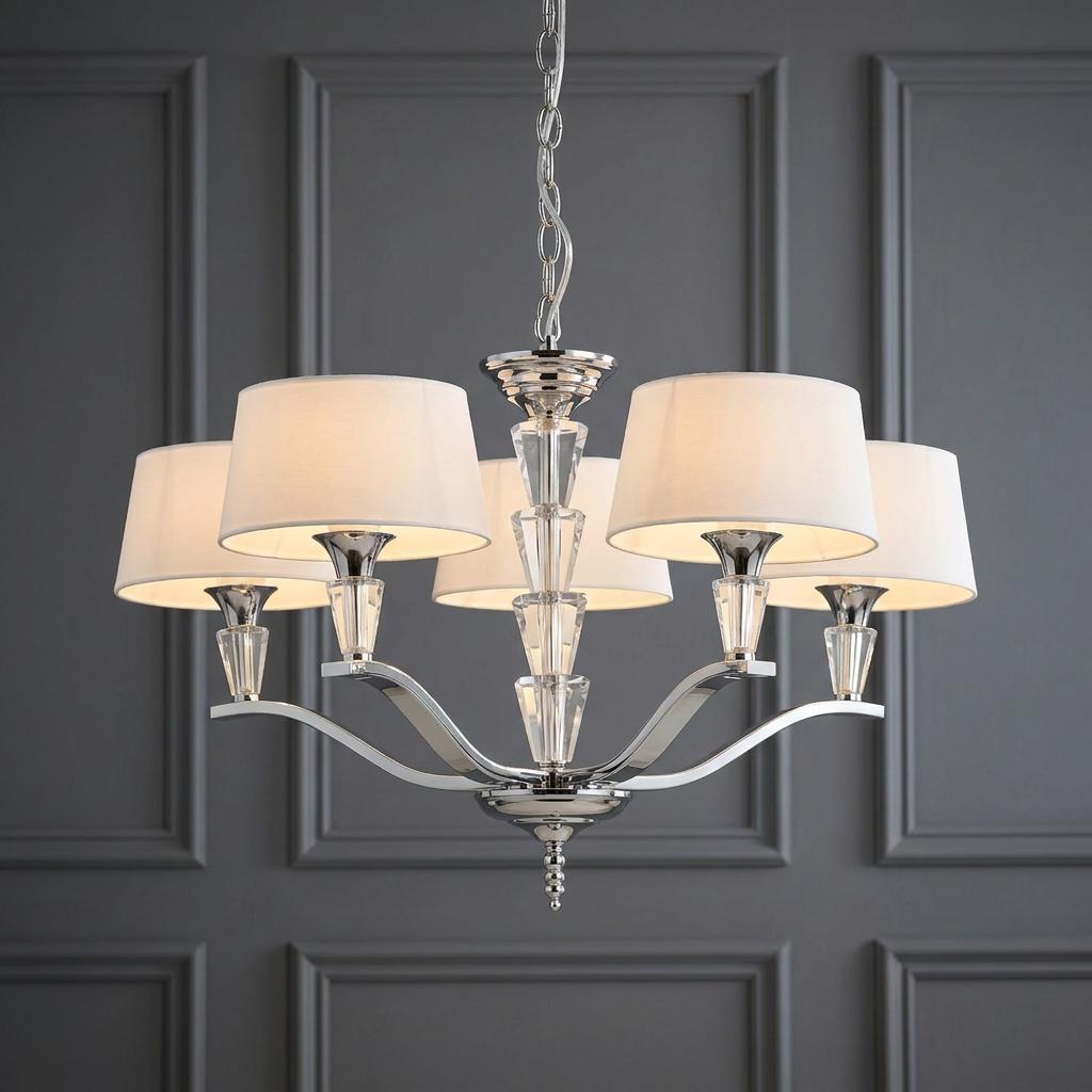 Five-light chrome chandelier with white fabric shades and crystal accents against a grey paneled wall.