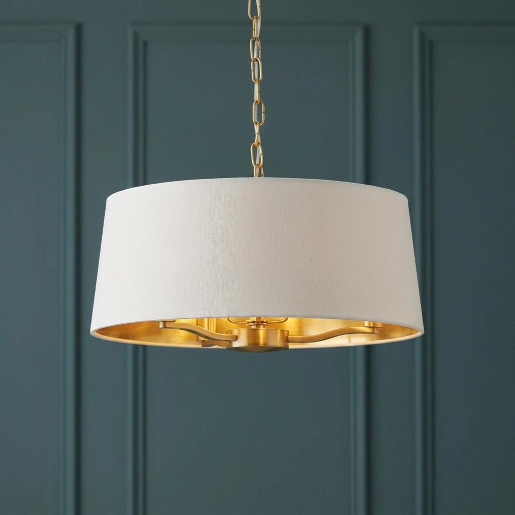 A satin gold 3-light pendant with a white drum shade and gold interior hanging against a teal paneled wall.