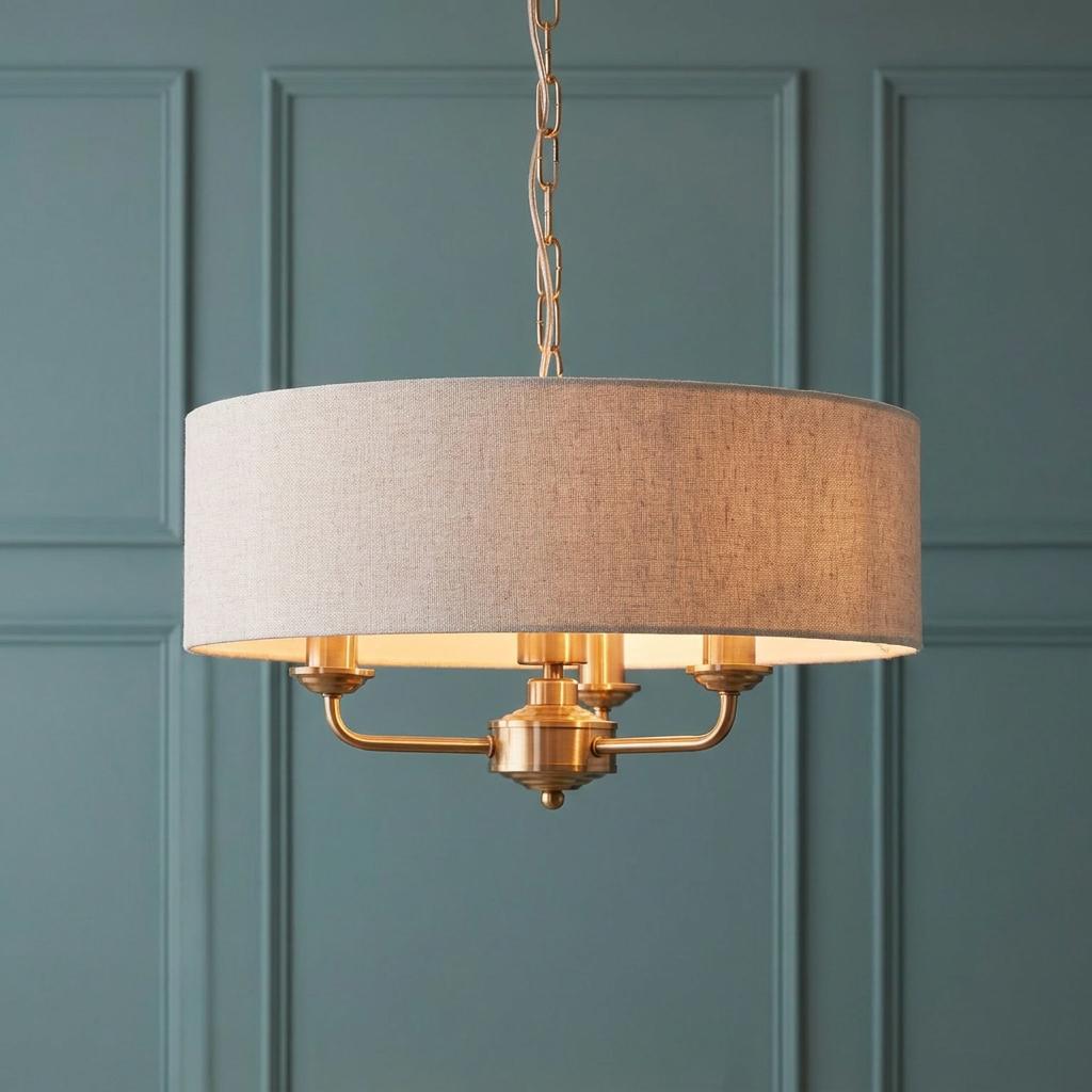 Aged brass 3-light pendant with a natural linen drum shade hanging against a teal paneled wall.