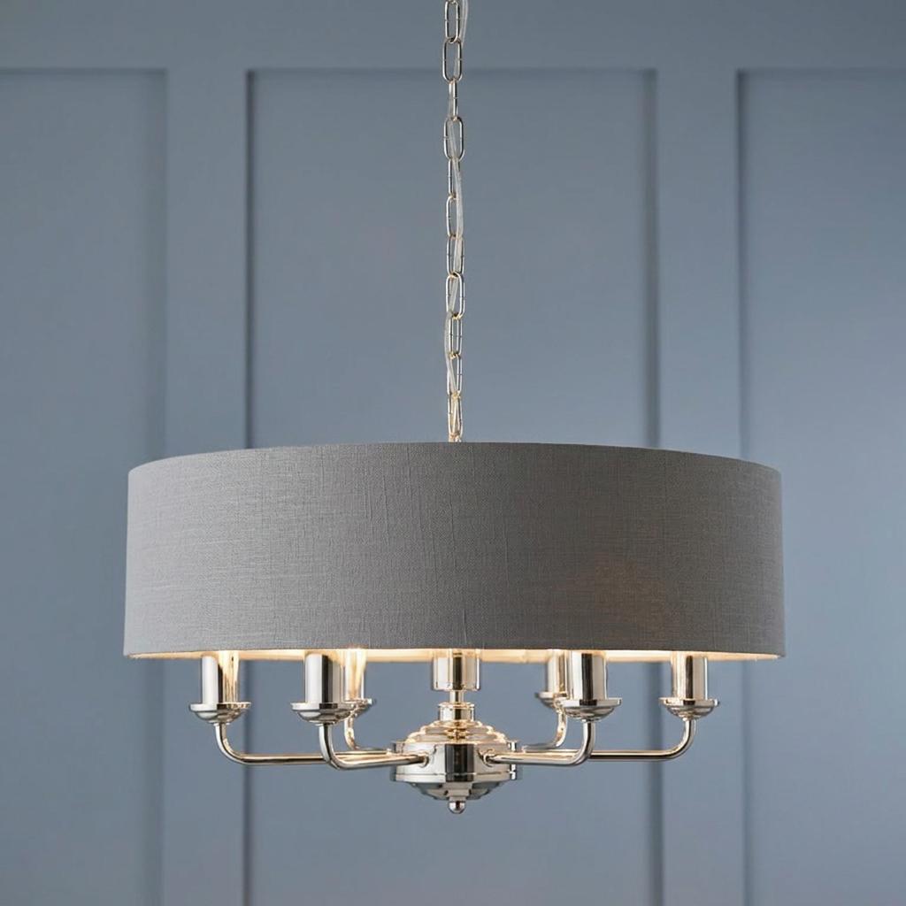 Six-light bright nickel pendant with a charcoal fabric drum shade against a blue paneled wall.