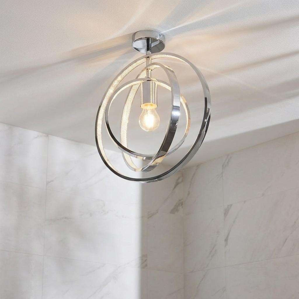 Modern chrome orbital ceiling light with interlocking LED rings and a central bulb against marble bathroom tiles.