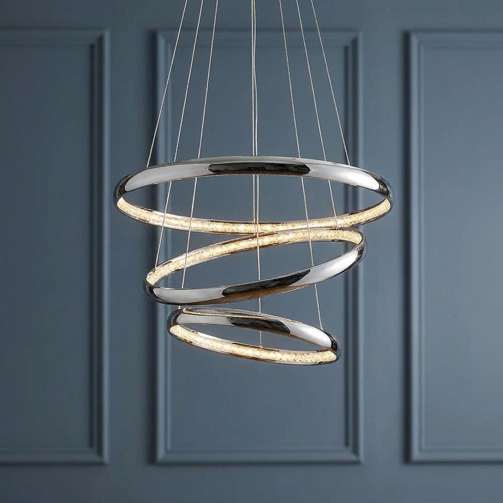 Three-tier chrome and crystal LED ring pendant light suspended against a blue wood-panelled wall.