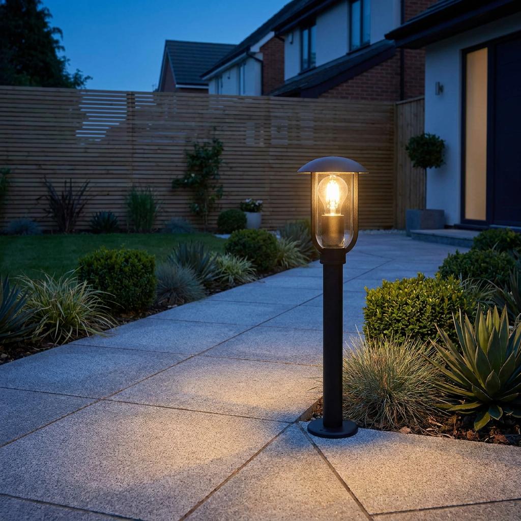 Black outdoor bollard light illuminating a stone garden path at twilight.