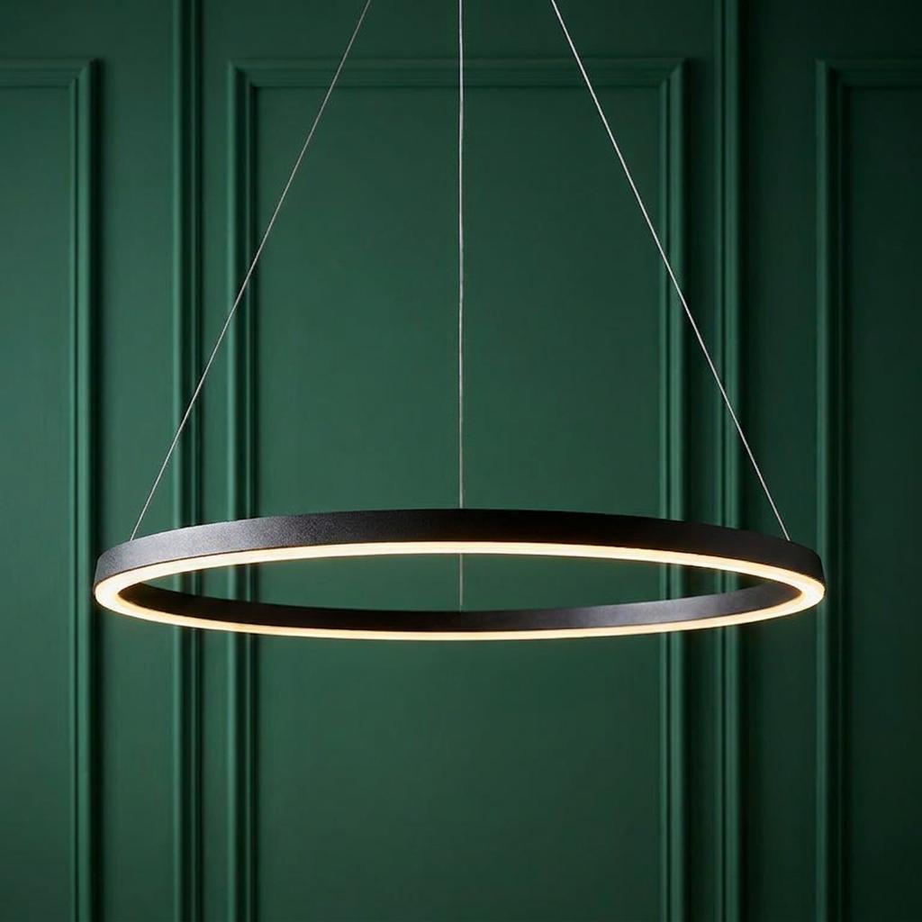 Minimalist black halo pendant light with a warm LED glow, set against a dark green panelled wall.