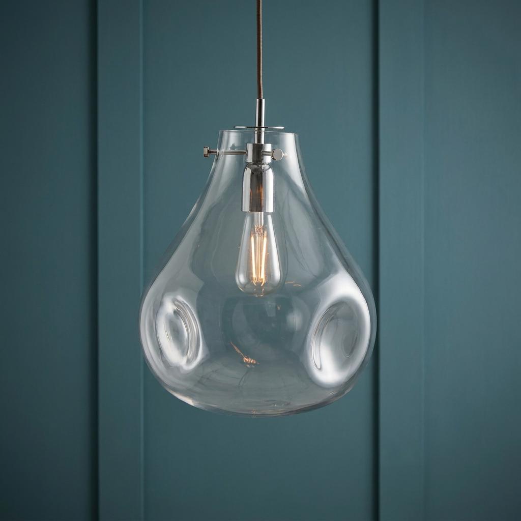 Clear pear-shaped glass pendant light with a filament bulb hanging against a teal paneled wall.