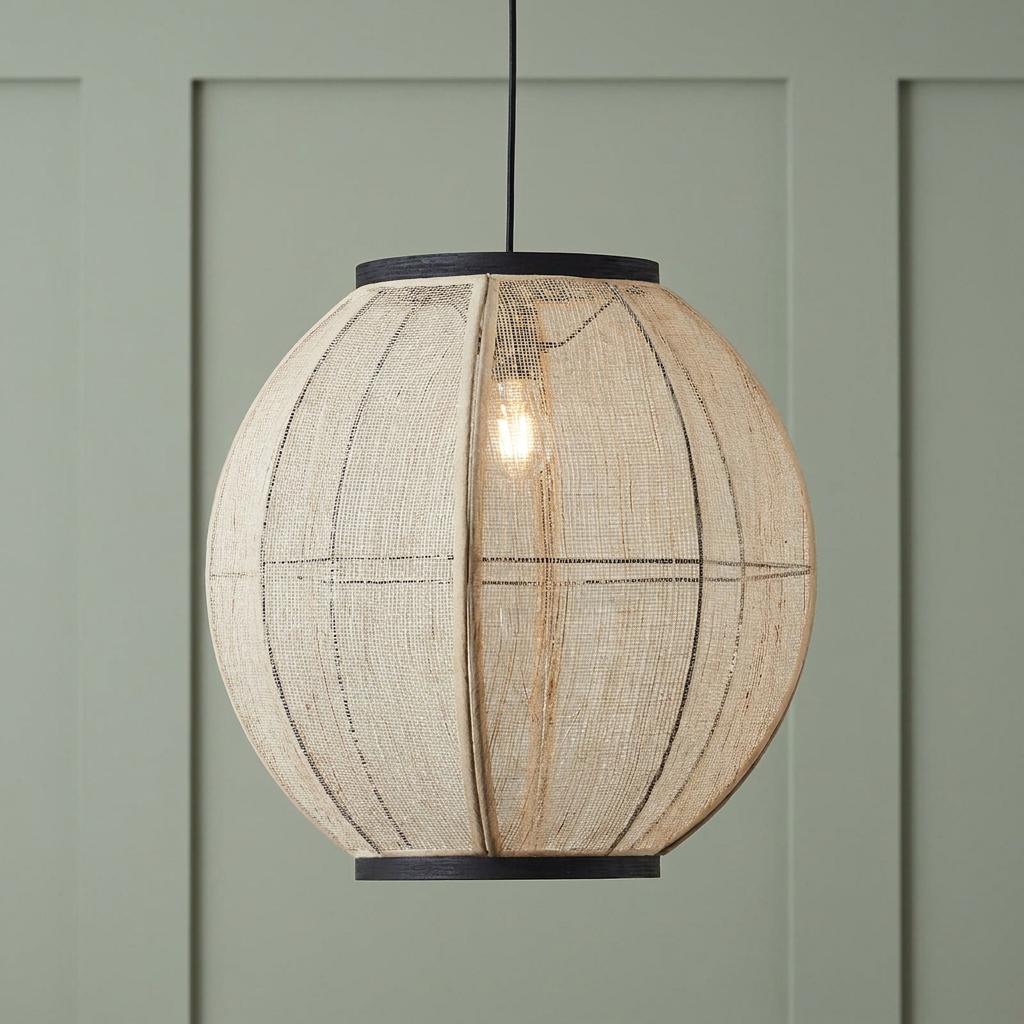 Natural linen globe pendant light with black trim, illuminated in front of a sage green paneled wall.