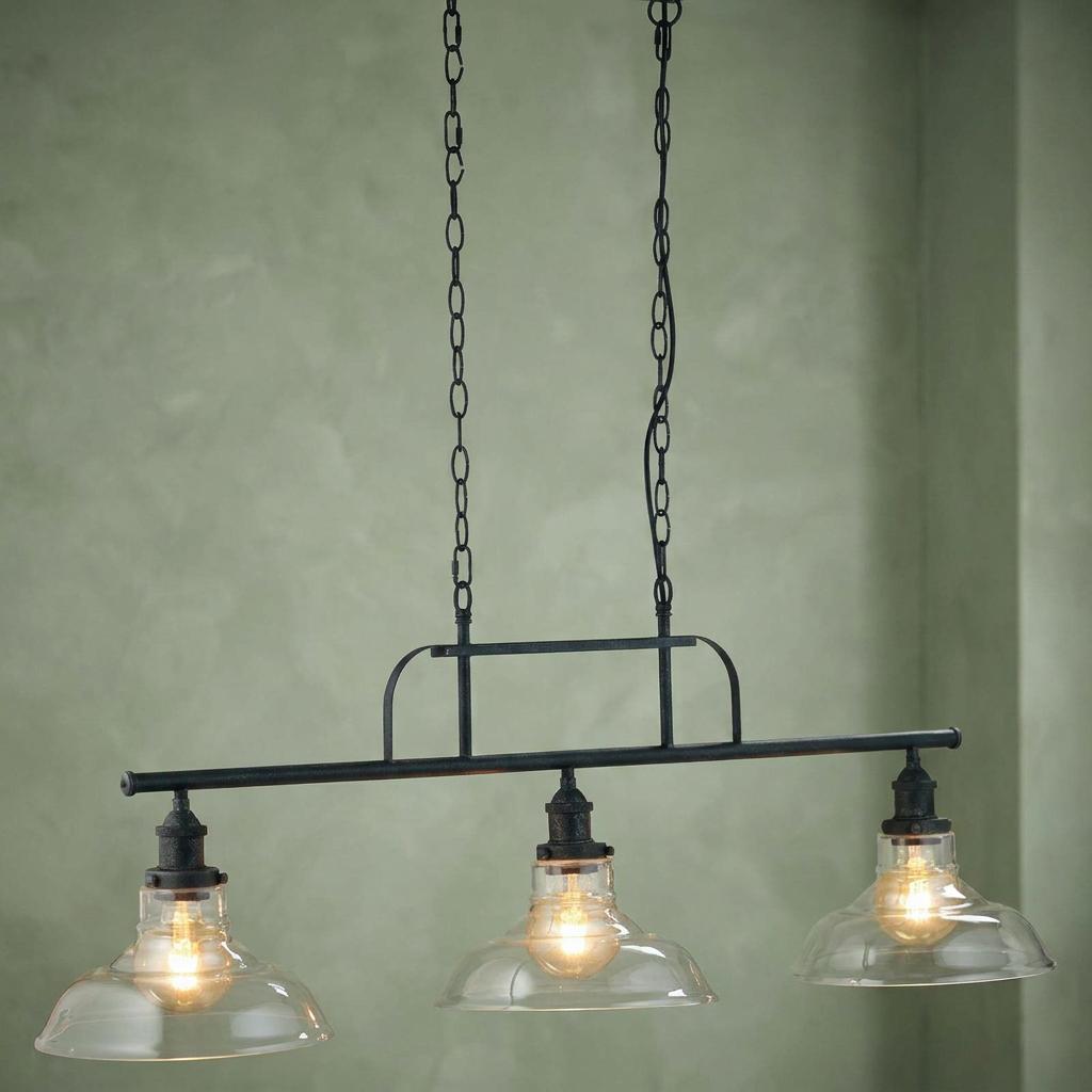 Three-light wrought iron bar ceiling fixture with clear glass shades hanging against a green wall.