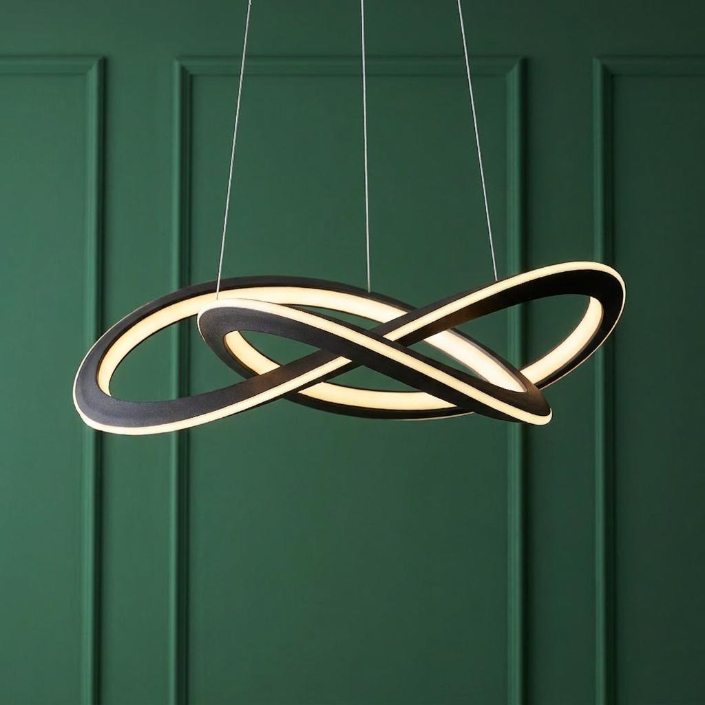 Black infinity knot LED pendant light illuminated against a dark green wood-paneled wall.