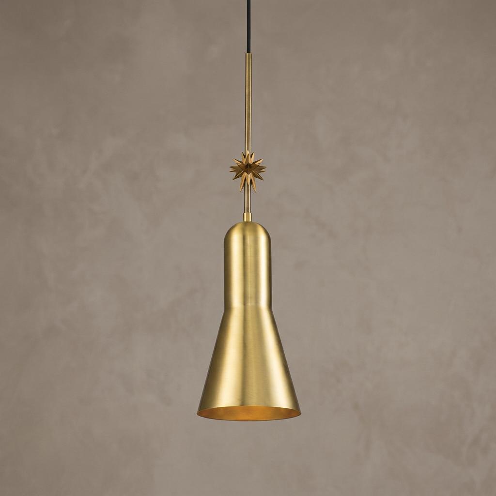 Aged brass pendant light with a conical shade and sunburst ornament against a textured neutral wall.