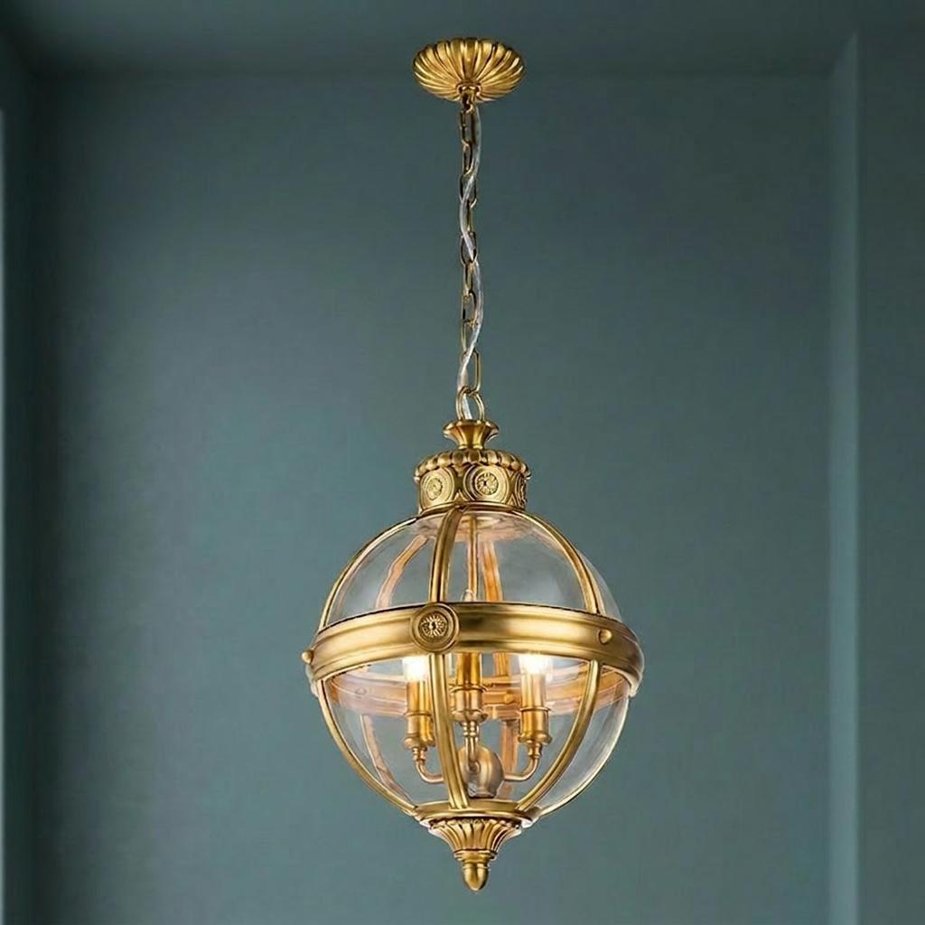 Feiss Adams 3-light pendant chandelier with a brushed brass globe frame and clear glass shade on a blue wall.