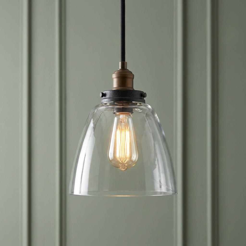 A Feiss Baskin 1-light pendant with clear glass bell shade and brass accents against a green panelled wall.