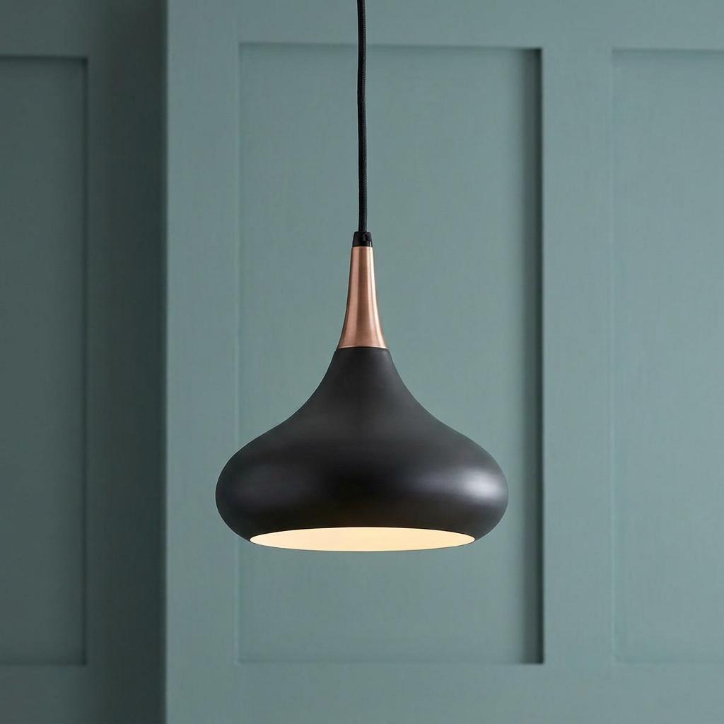 Matte black and copper teardrop pendant light hanging against a green paneled wall.