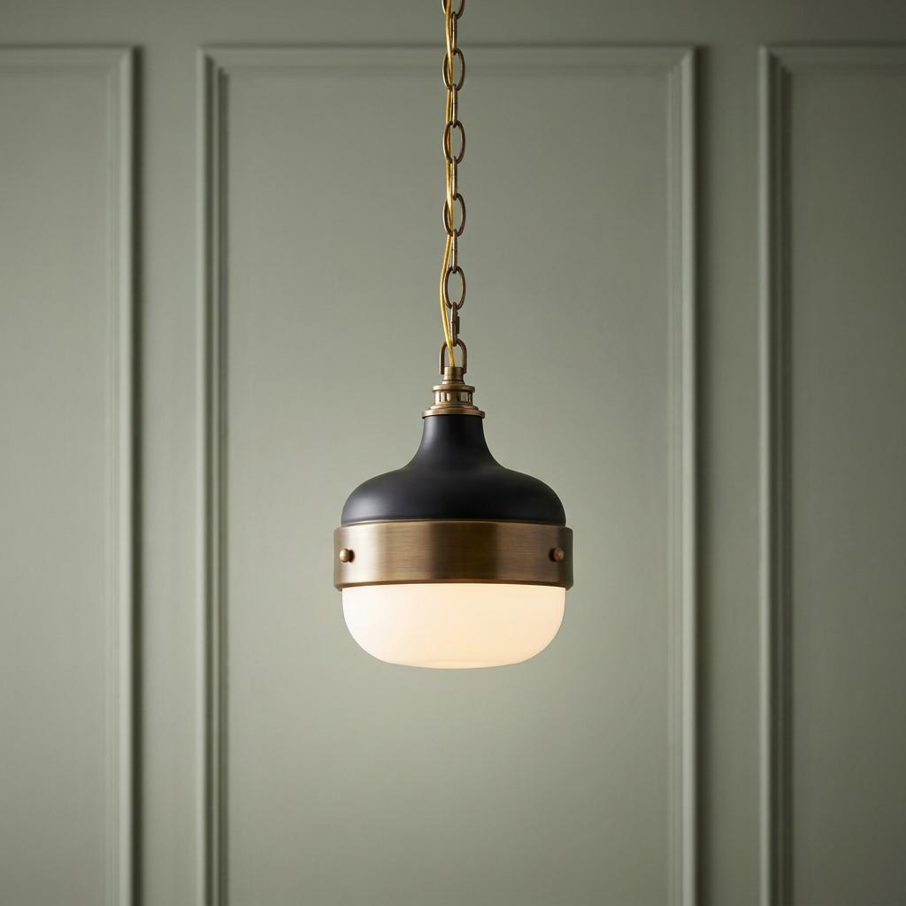 Feiss Cadence mini pendant light with black and brass metalwork and opal glass, hanging against a green paneled wall.