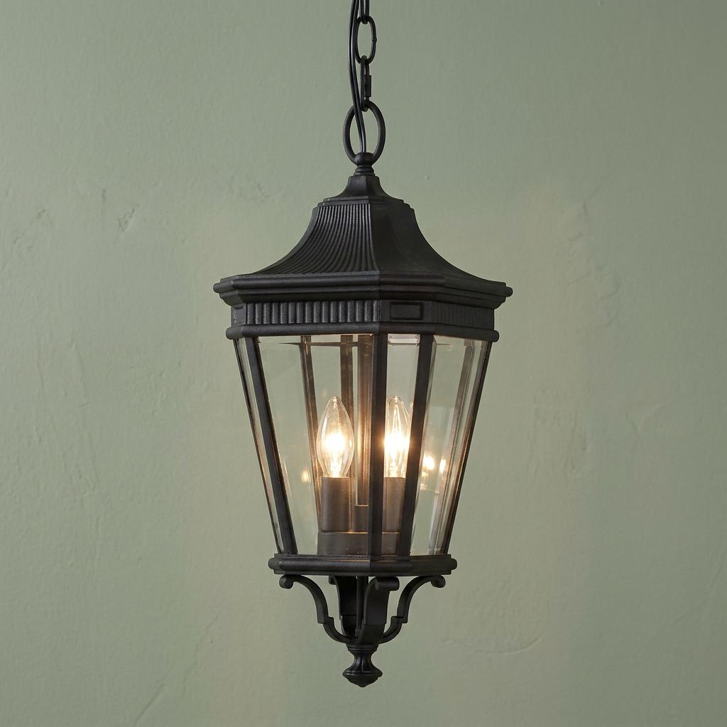 Traditional black outdoor lantern pendant with clear glass and two lit candle bulbs against a sage green wall.
