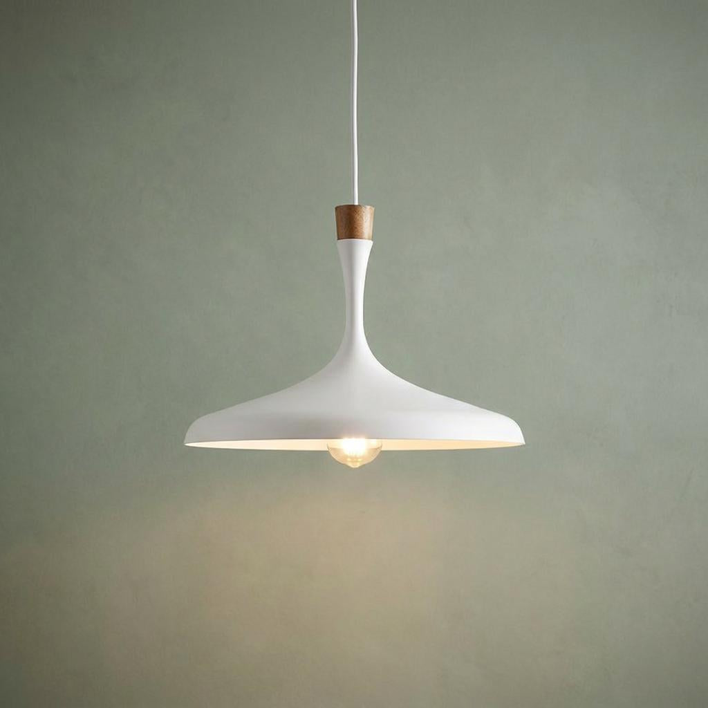 A matte white pendant light with a wood accent and warm bulb, hanging against a muted green wall.