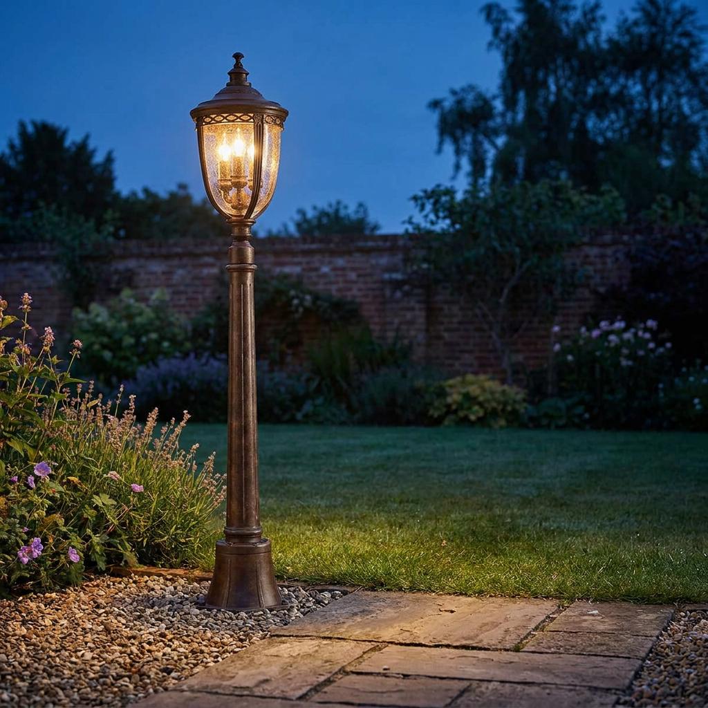 Bronze outdoor pedestal lantern with seeded glass glowing in a twilight garden setting.