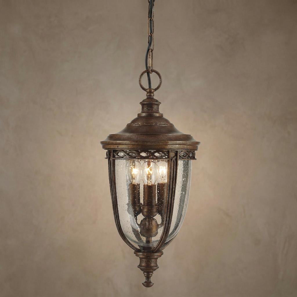 Bronze outdoor pendant lantern featuring seeded glass and three candle-style bulbs against a neutral wall.