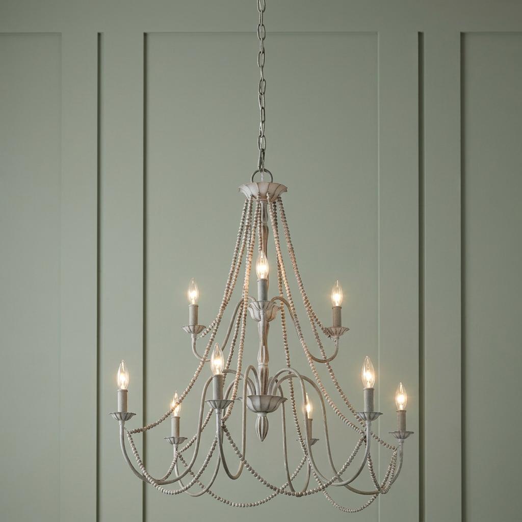 Distressed grey 9-light chandelier with decorative bead drapes against a light green paneled wall.