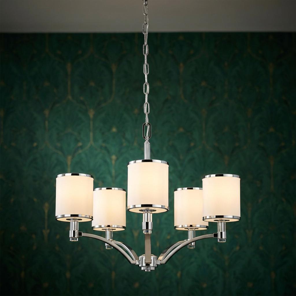 Five-light chandelier with white drum shades and chrome hardware against a green patterned wall.