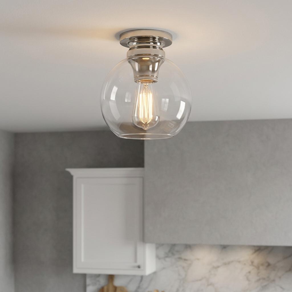 Polished nickel flush mount ceiling light with a clear glass globe and glowing Edison bulb in a modern interior.