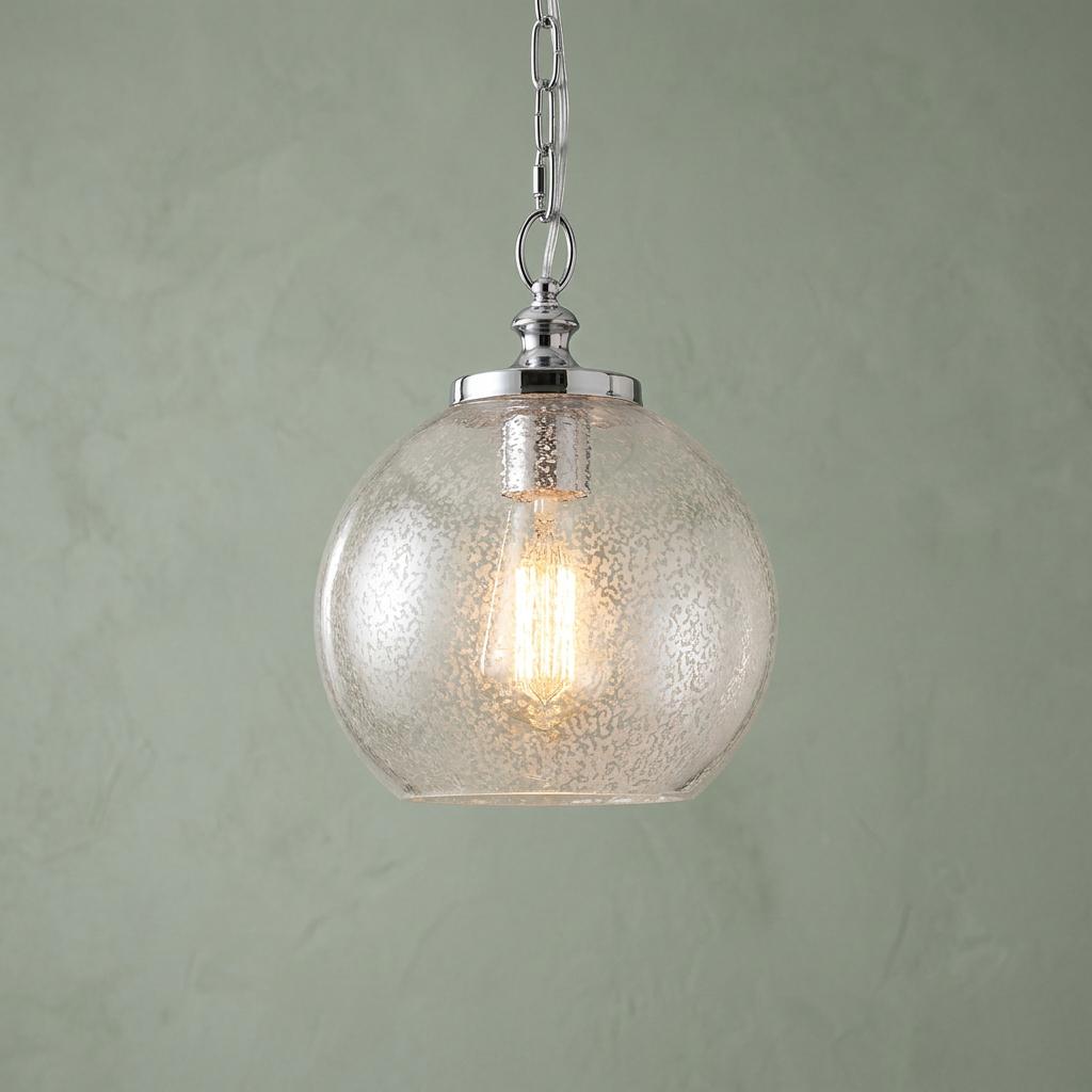 A Feiss Tabby pendant light with a seeded glass globe shade and glowing Edison bulb against a green wall.