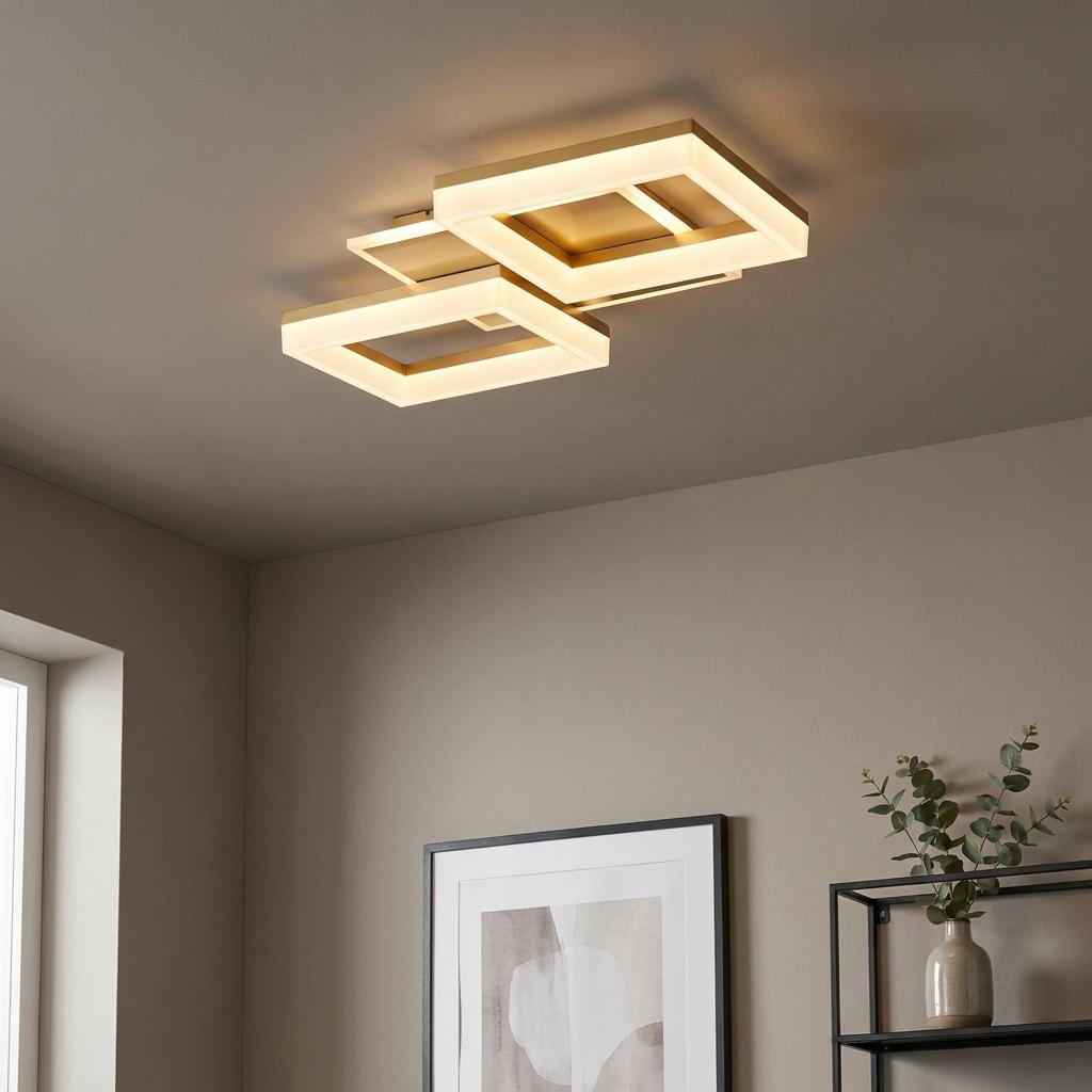Modern gold flush ceiling light with two interlocking square frames emitting a warm glow in a neutral-toned room.