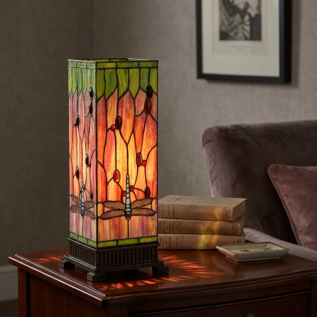 Square Tiffany table lamp with a green and amber dragonfly stained glass design glowing on a wooden side table.