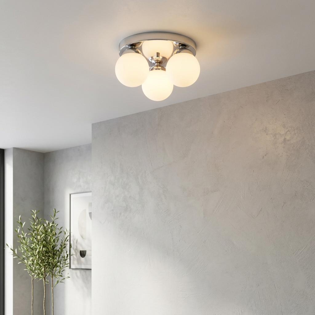 A modern chrome flush ceiling light with four white globe shades glowing on a white ceiling in a contemporary room.
