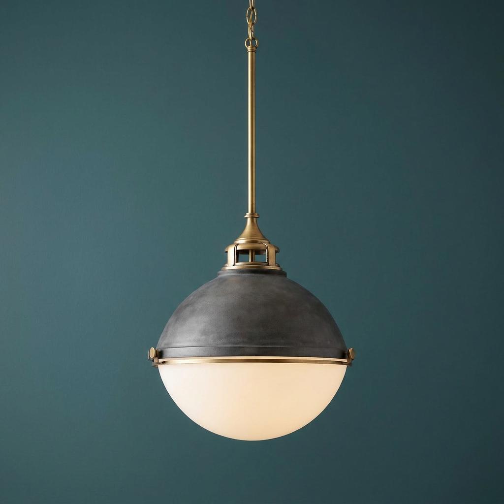 A zinc and brass spherical pendant light with a frosted glass lower half against a dark teal wall.