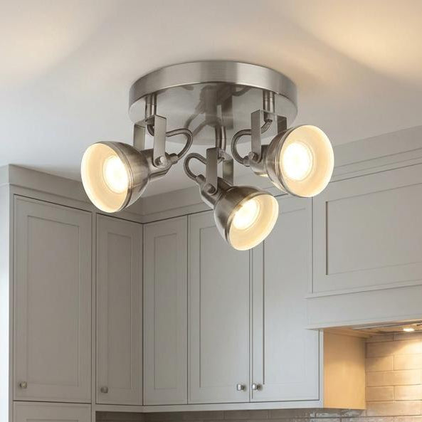 Three adjustable satin silver spotlights illuminate a modern white kitchen island with a bowl of fruit.