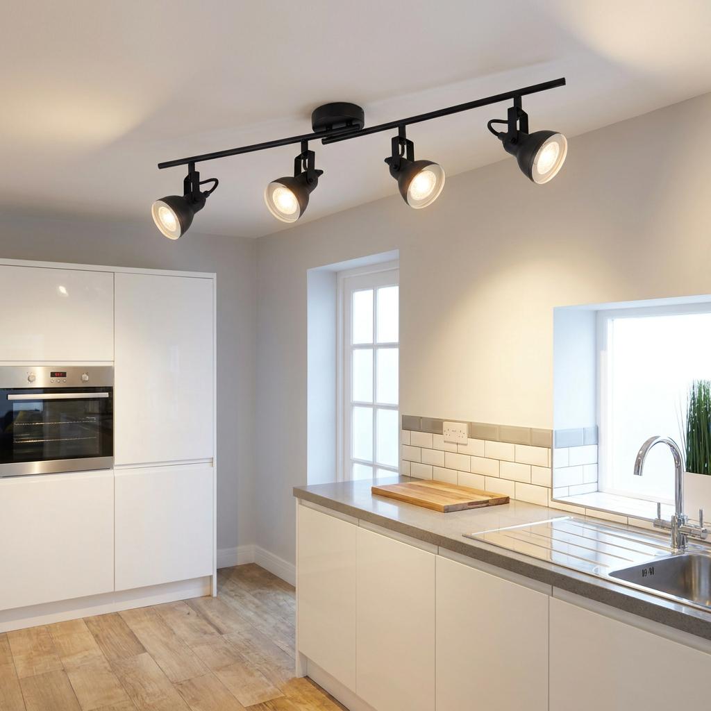 Four black adjustable spotlights on a ceiling bar illuminate a modern white kitchen.