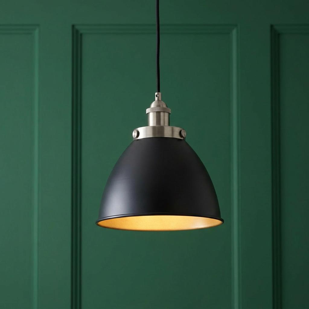 Industrial pewter pendant light with a black dome shade and warm glow against a green paneled wall.