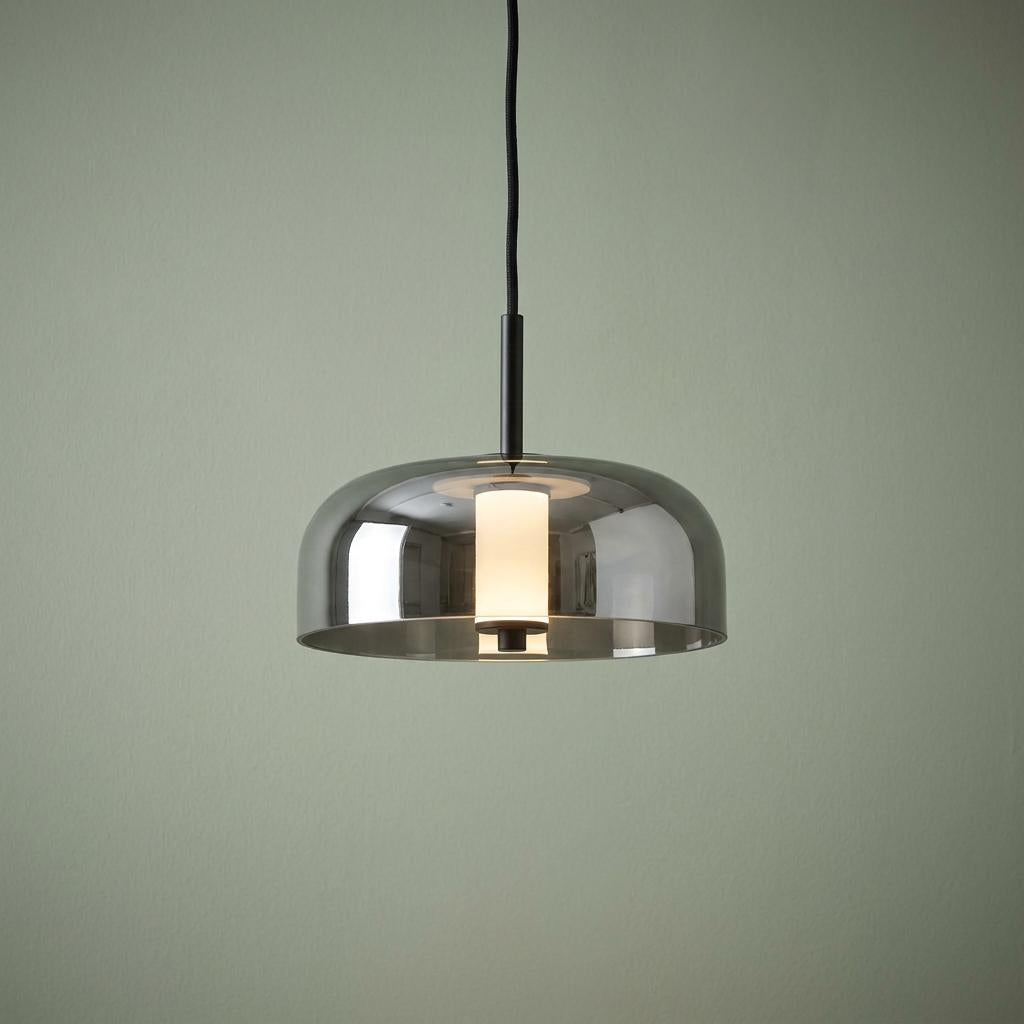Frisbee 1 Light LED Black Pendant with a smoked glass shade and glowing internal diffuser against a green wall.