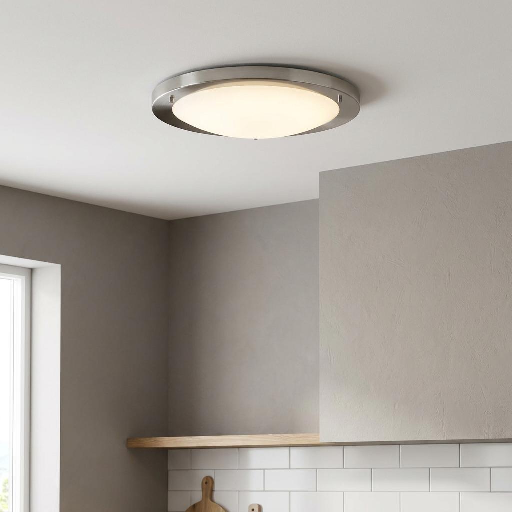 A silver flush ceiling light with glowing opal glass mounted on a white ceiling in a modern kitchen.
