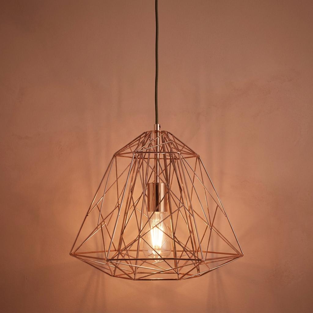 Copper geometric cage pendant light with a single bulb against a textured pink wall.