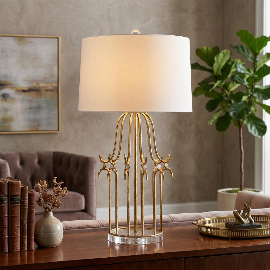 Gilded Nola Stella table lamp with a distressed gold cage-style base and white shade in a living room setting.