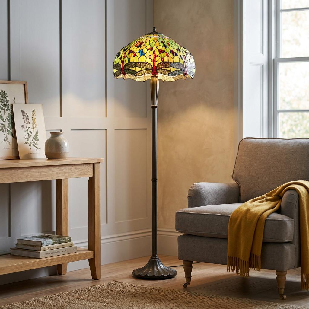 Green and yellow dragonfly Tiffany floor lamp standing next to a grey armchair in a cozy living room.