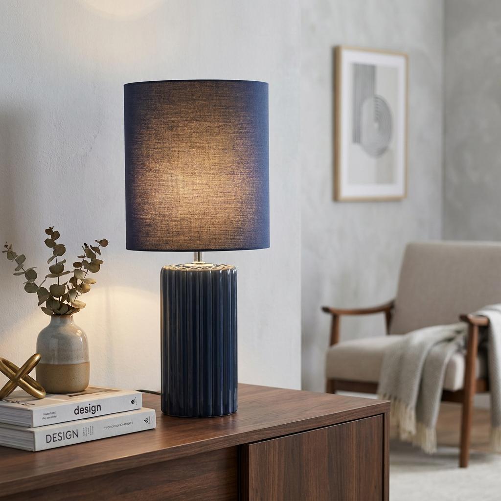 Navy blue fluted ceramic table lamp with a matching fabric drum shade on a wooden cabinet in a living room.