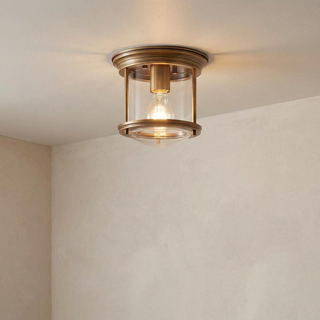 Brushed bronze flush mount ceiling light with clear glass shade illuminated against a neutral ceiling.