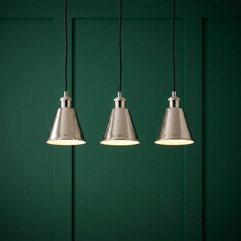 Three lit polished nickel conical pendant lights suspended against a dark green paneled wall.