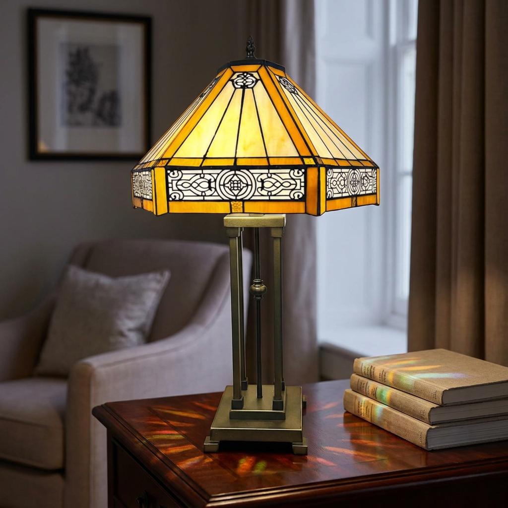 Halcyon Tiffany Table Lamp with a yellow stained-glass shade and bronze base on a wooden table with books.