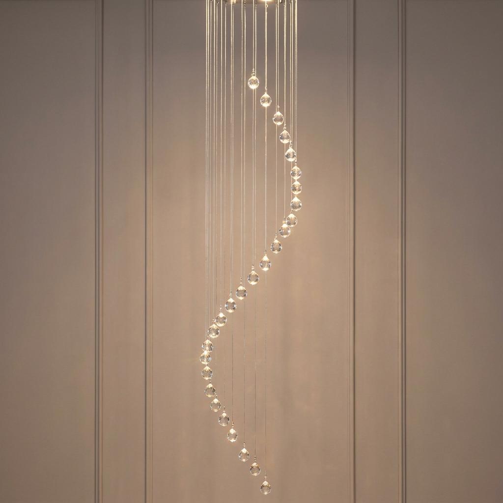 Cascading pendant light with crystal spheres forming a spiral shape against a neutral paneled wall.