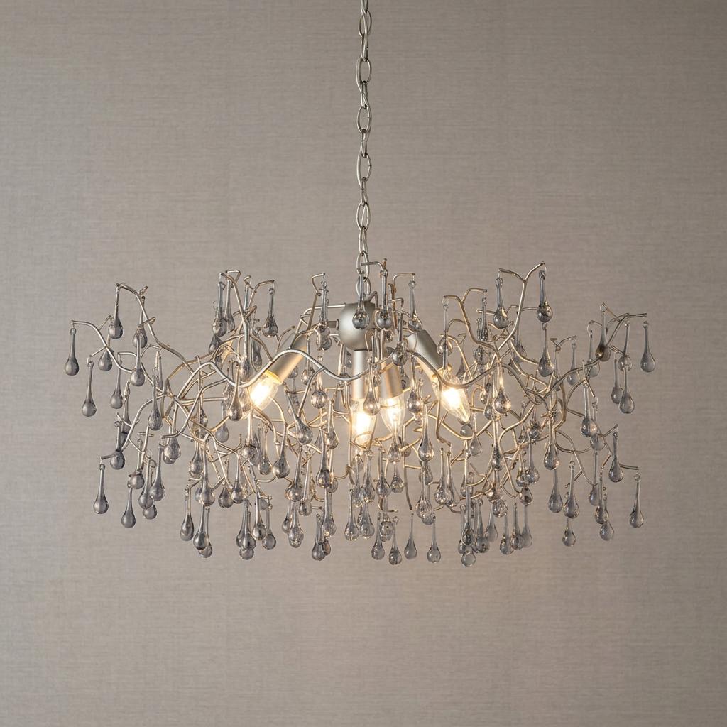 A silver branching pendant light with four glowing bulbs and cascading glass teardrops against a neutral wall.