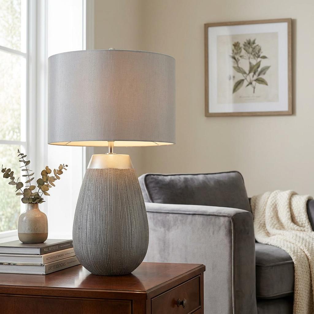 Grey textured ceramic table lamp with a matching fabric shade on a wooden side table in a cozy living room.